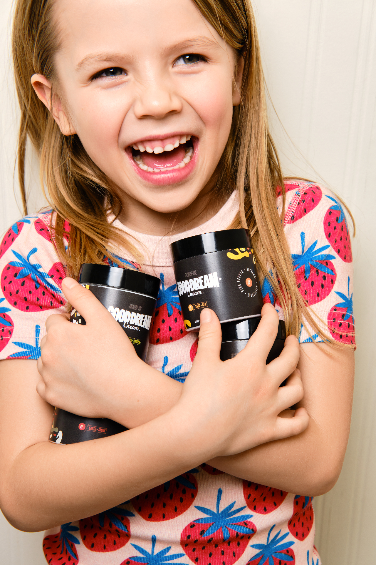 A laughing child hugging three jars of Good Dream Cream™